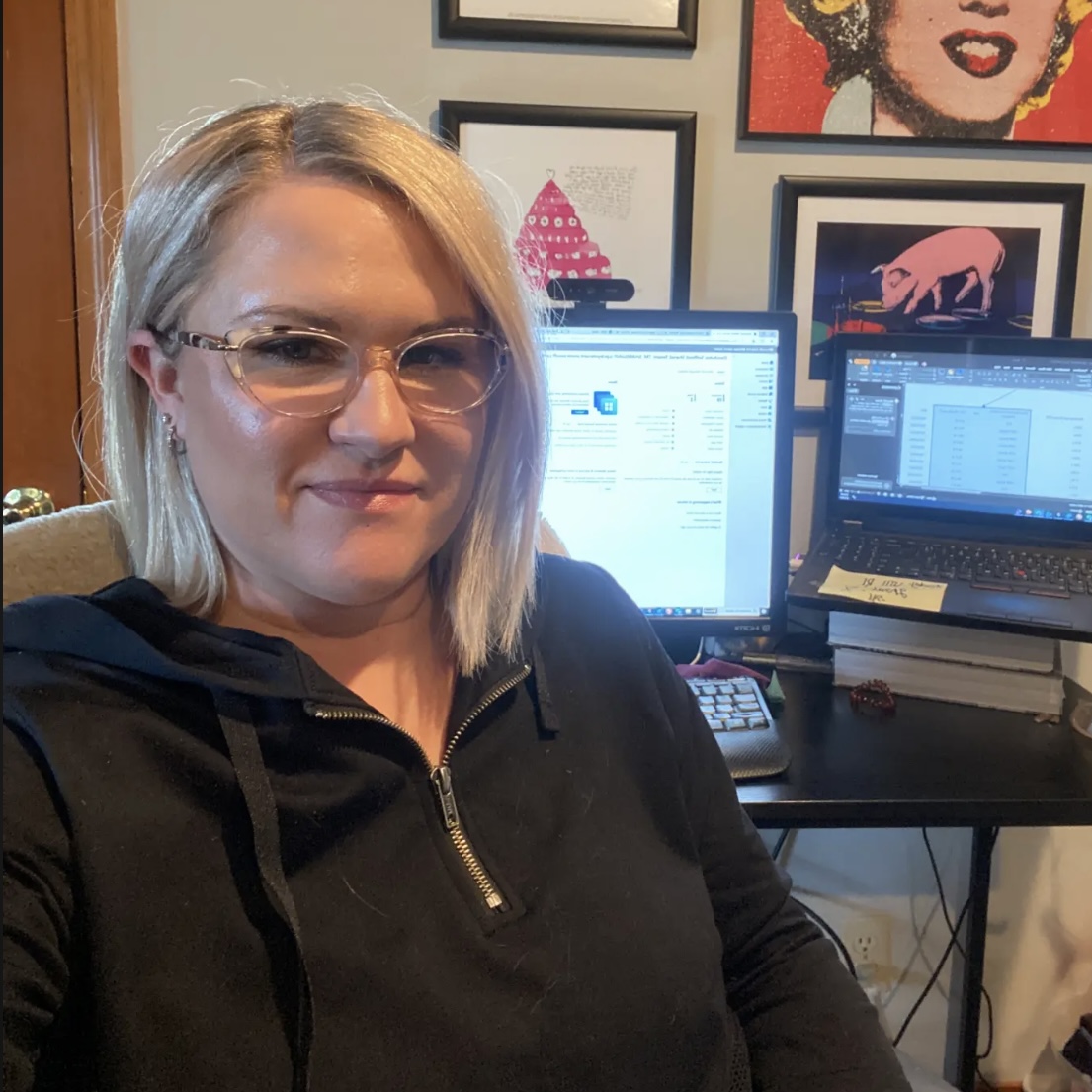 Amanda at her home desk, with a small gallery of pop-art prints on the wall behind her